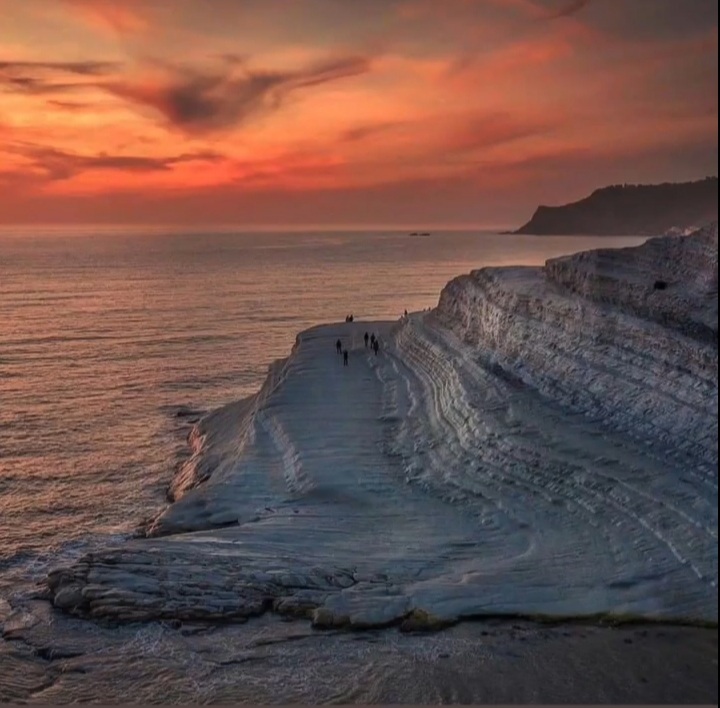 Persone passeggiano sulla Scala dei Turchi al tramonto, con il cielo infuocato